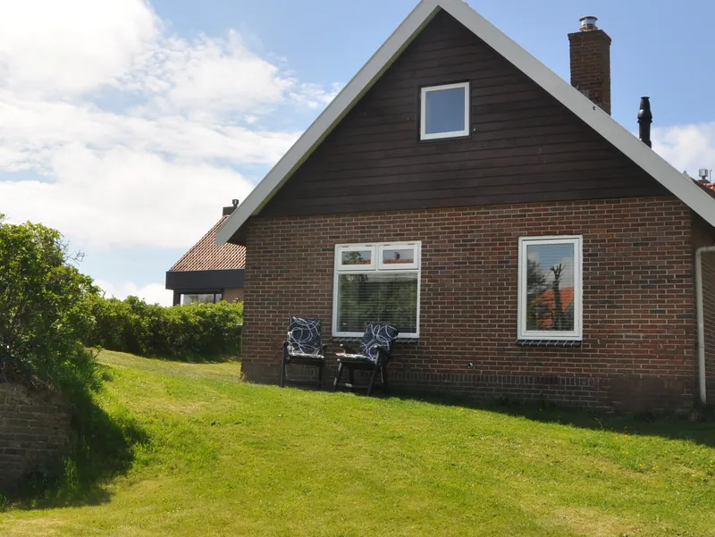 Het huis vanuit de tuin: een grasveld in de zon, en twee tuinstoelen tegen de muur.
