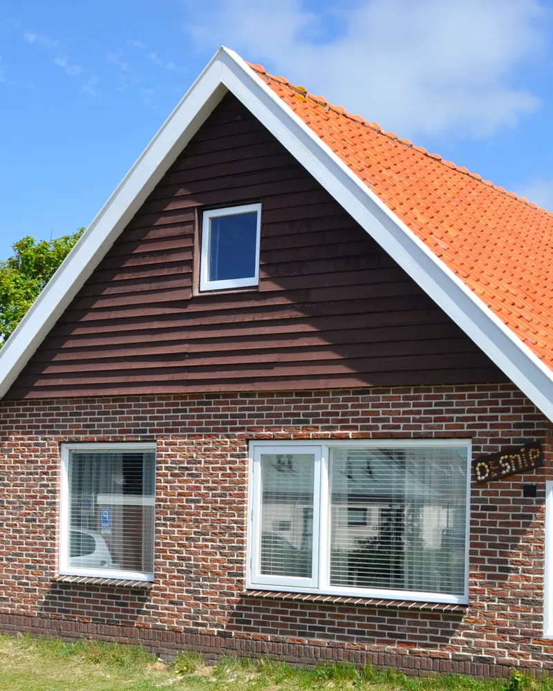 De voorkant: een donkere houten gevel met één raampje onder oranje dakpannen, en De Snip op een bordje naast het grote raam.